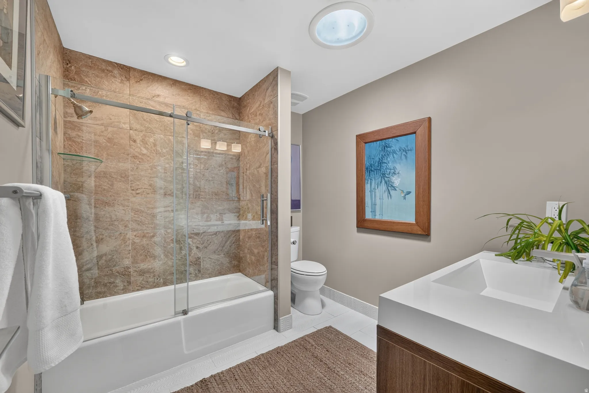 Modern bathroom featuring a built-in tub with a glass sliding door, stone-look wall tiling, and a recessed light fixture