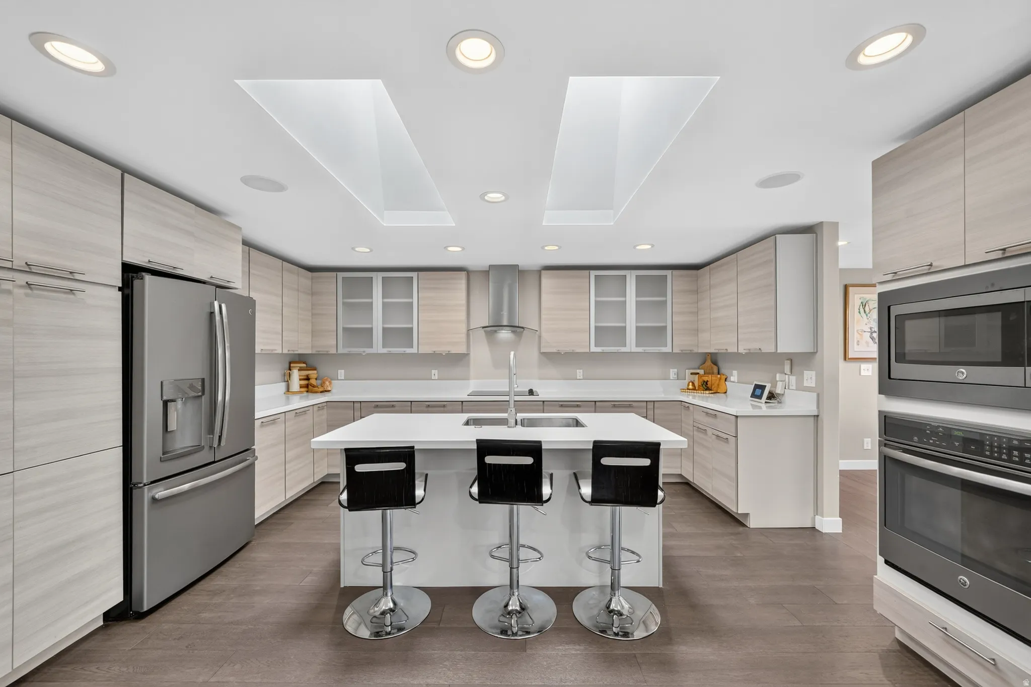 Kitchen featuring a central island, light wood-finish cabinetry, stainless steel appliances, recessed lighting, and two skylights
