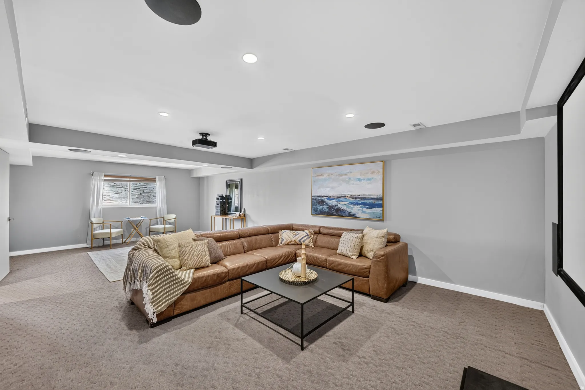 Spacious carpeted room featuring recessed lighting, a ceiling-mounted projector, and a large projection screen