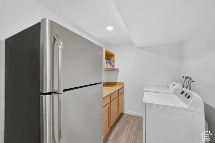 Utility space featuring a stainless steel refrigerator, light wood-finish cabinetry with a countertop, and wood-finish flooring