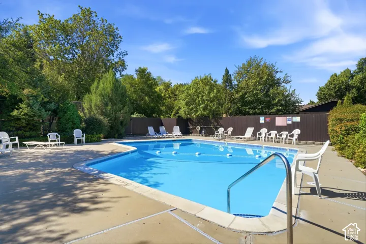 Outdoor swimming pool with concrete decking, perimeter fencing, and mature trees