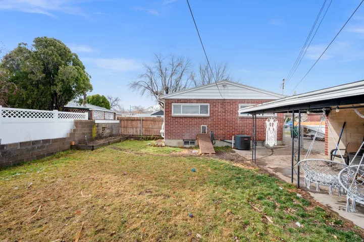 Expansive backyard featuring a brick exterior, concrete patio, white lattice fencing, and a retaining wall