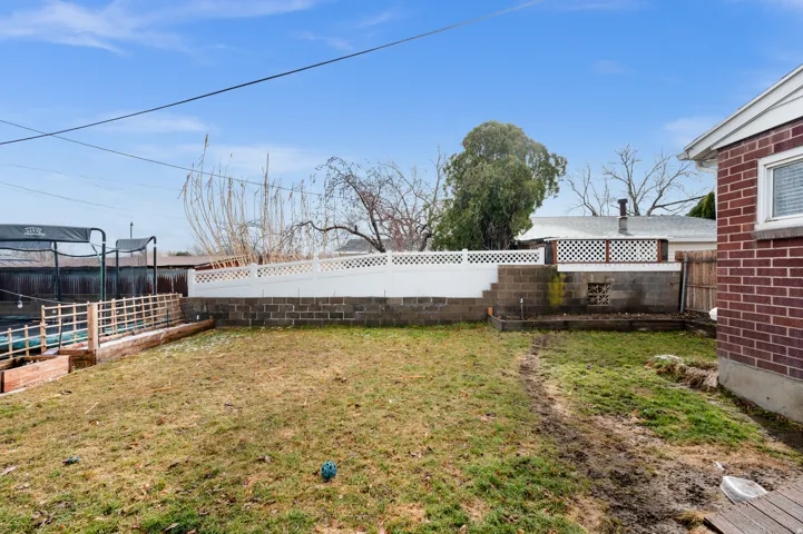 Expansive backyard featuring a tiered retaining wall with white lattice fencing, a raised garden bed with a wood rail, and a red brick exterior wall