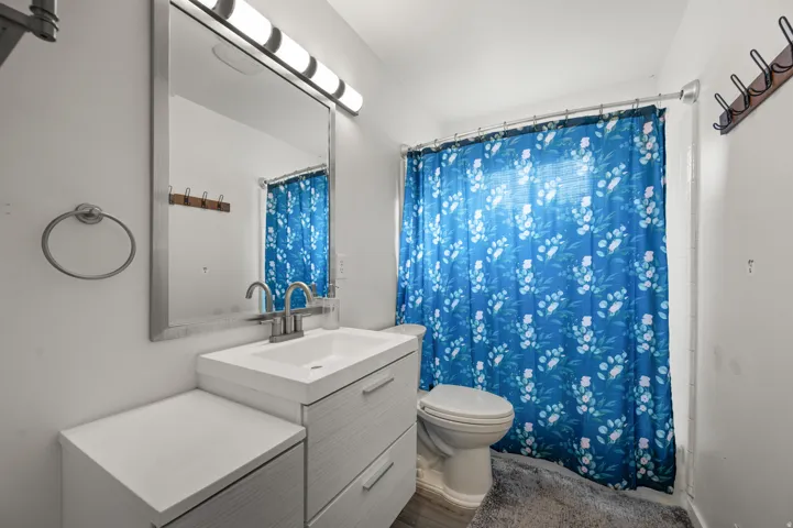 Bathroom featuring a modern vanity with integrated sink, rectangular mirror, contemporary wall-mounted light fixture, and a toilet