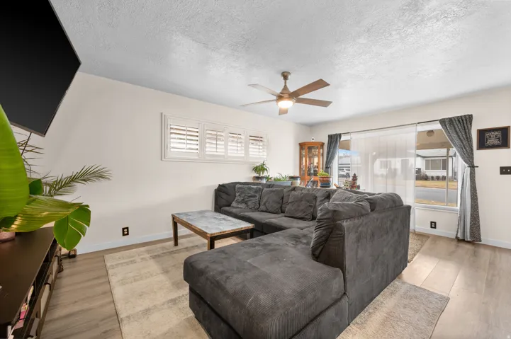 Living area featuring wood-finish flooring, white plantation shutters, and a ceiling fan