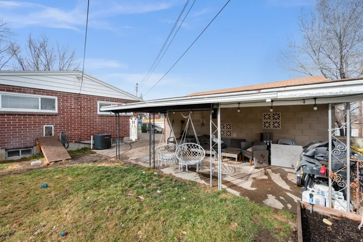 Expansive backyard featuring a covered patio with string lighting, a concrete block wall, decorative wall cutouts, and a sloped lawn area