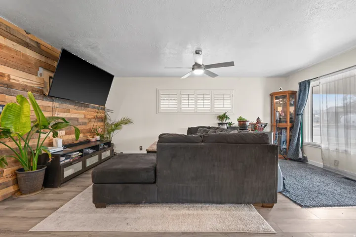 Living area featuring a prominent wood-panel accent wall, wood-finish flooring, and a ceiling fan with integrated lighting