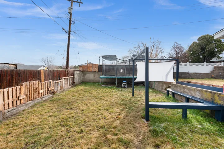Expansive backyard featuring a grass lawn, privacy fencing, a multi-level retaining wall, and a metal structure with a white shade sail
