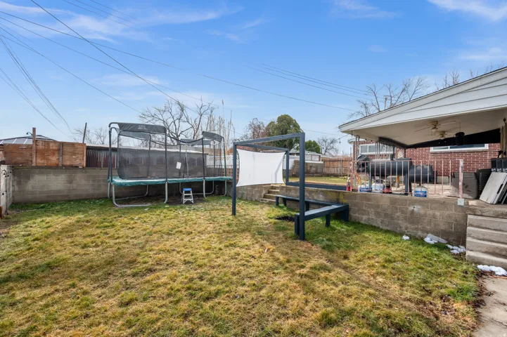Expansive backyard featuring a concrete block retaining wall, a paved patio area, and a covered porch with a ceiling fan