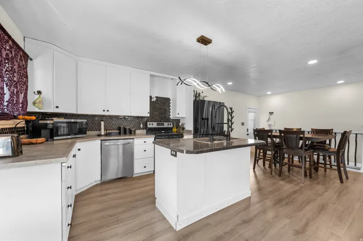 Open-concept kitchen featuring white cabinetry, a hexagonal tile backsplash, and a central island with a sink