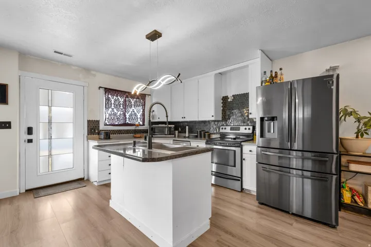 Contemporary kitchen featuring white cabinetry, dark countertops, and a central island with an integrated sink
