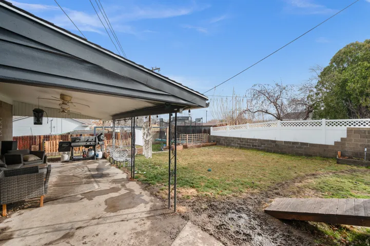 Covered patio with concrete flooring, supported by metal posts, offering an exterior ceiling fan