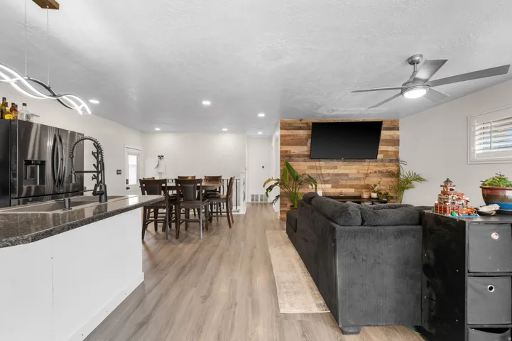 Open-concept living area featuring wood-finish flooring, a kitchen island with stone countertop, stainless steel appliances, and a wood-paneled accent wall