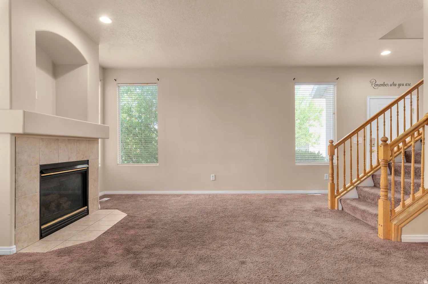 Living space featuring a tile-surround fireplace with hearth, a built-in arched alcove, recessed lighting, and two windows with blinds