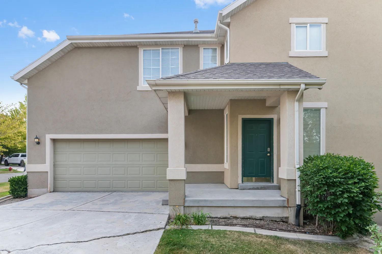 Stucco exterior featuring a covered entry, dark green front door, and an attached two-car garage