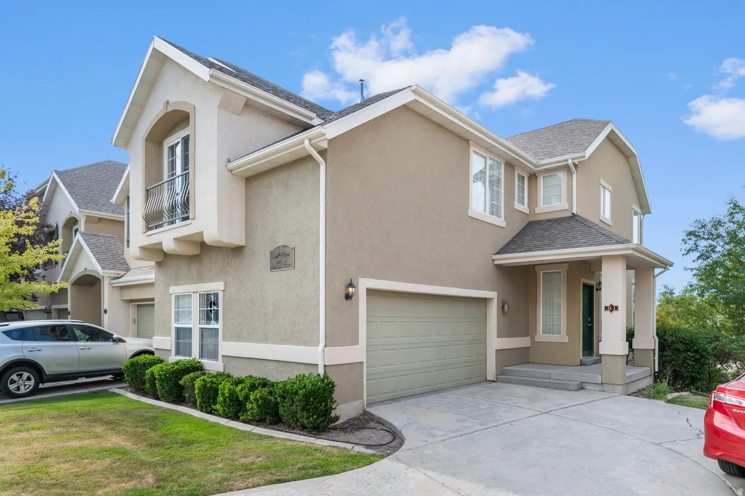 Stucco exterior with a peaked roofline, front-facing garage, covered entryway, and a Juliet balcony
