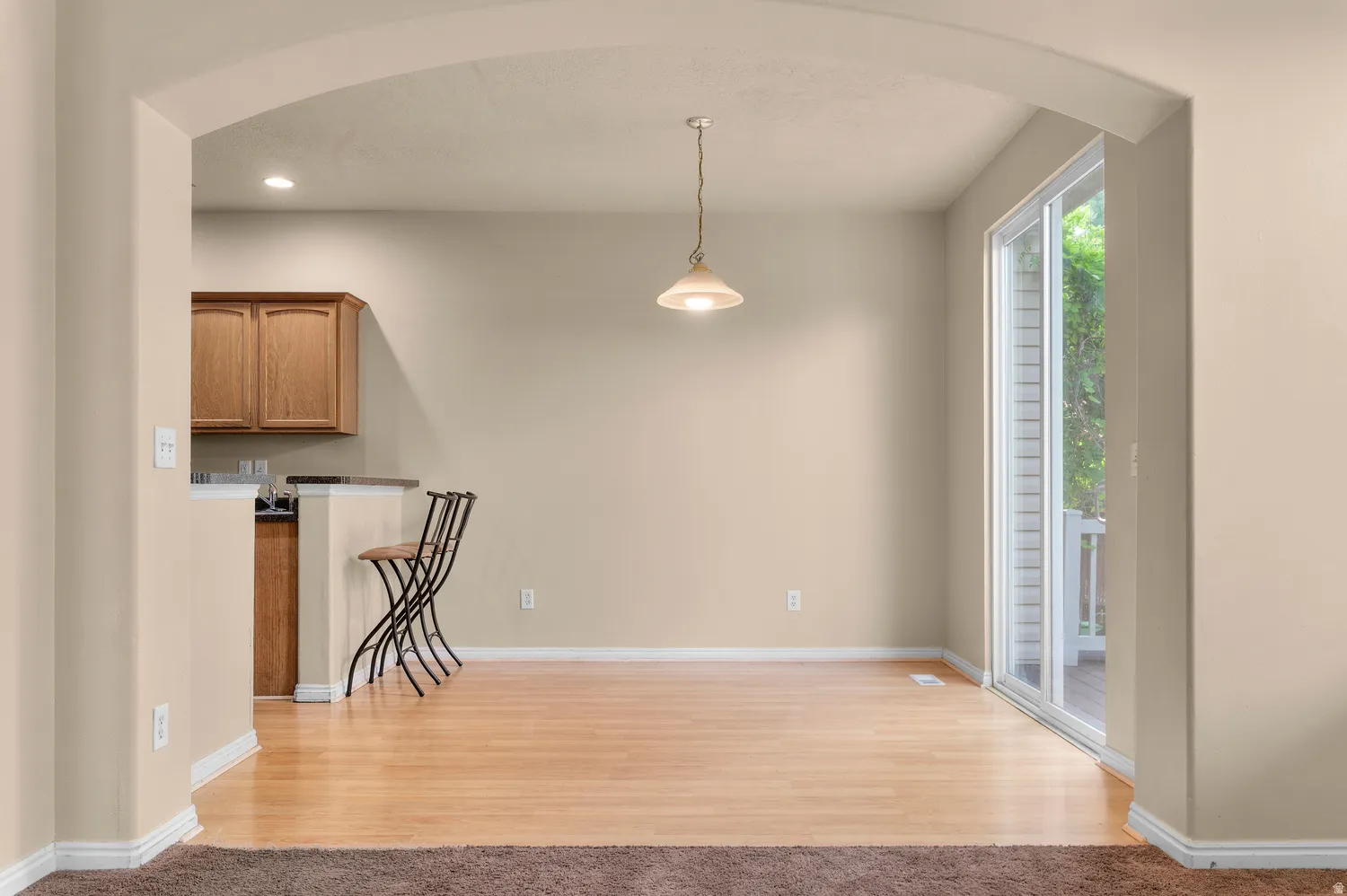Bright dining area featuring wood-finish flooring, a pendant light fixture, and a sliding glass door providing access to an outdoor balcony