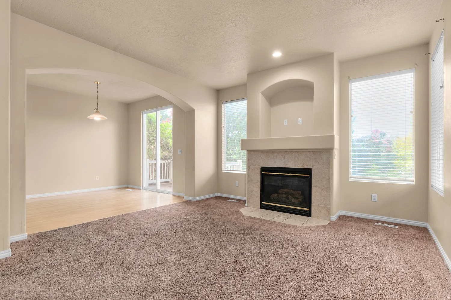 Living room featuring a corner fireplace with a tile surround and mantel, built-in niche, and large windows with blinds