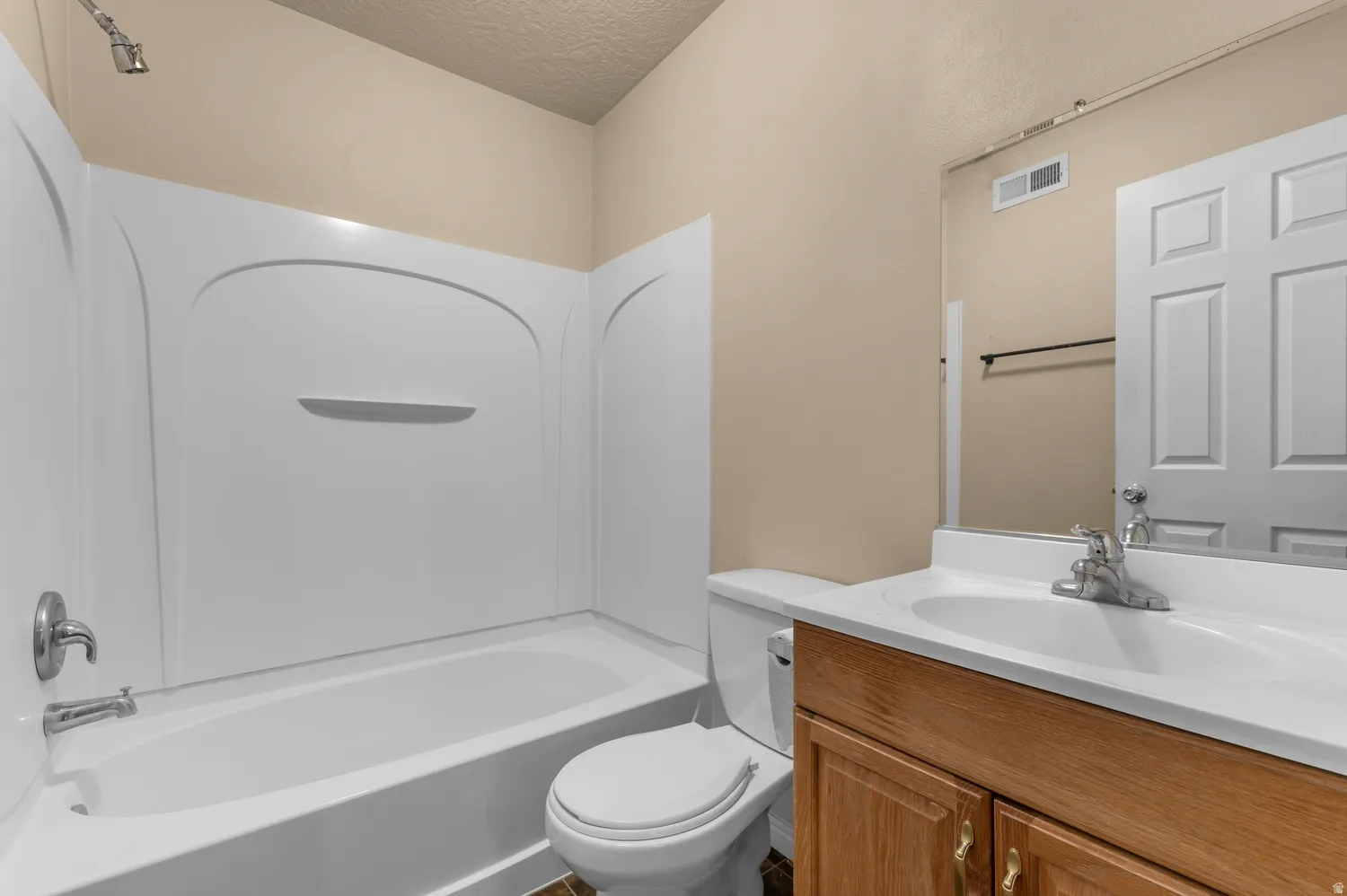 Bathroom featuring a tub/shower combination with a white surround, a toilet, a wood-finish vanity with a white countertop and integrated sink, and a framed wall mirror