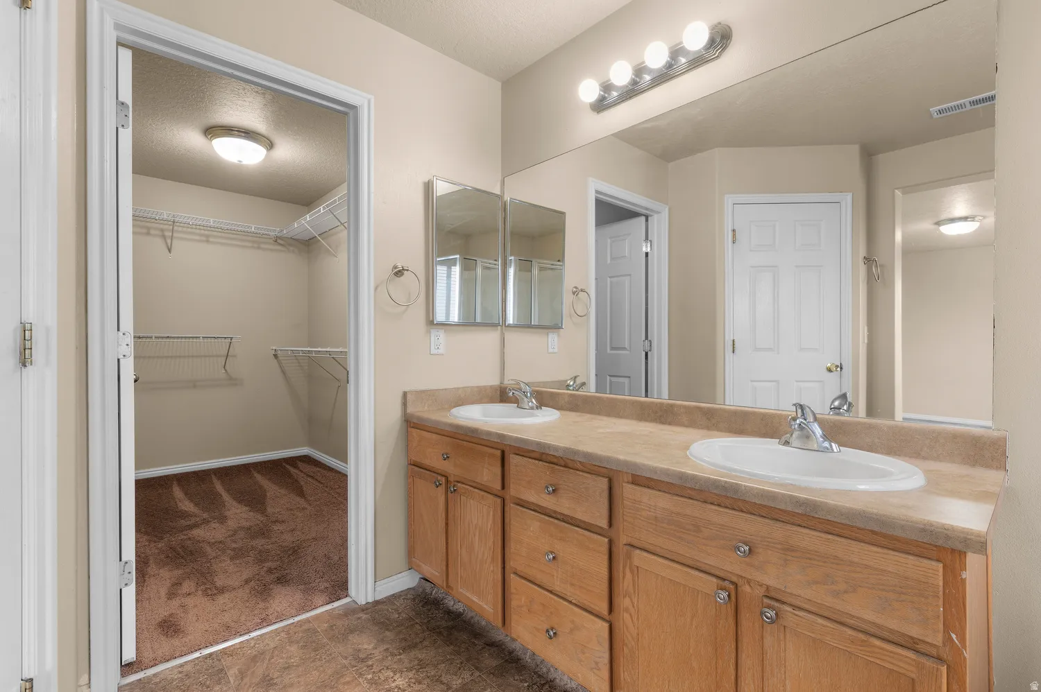 Dual vanity with light wood-finish cabinetry and integrated sinks, featuring a full-width mirror and polished chrome fixtures