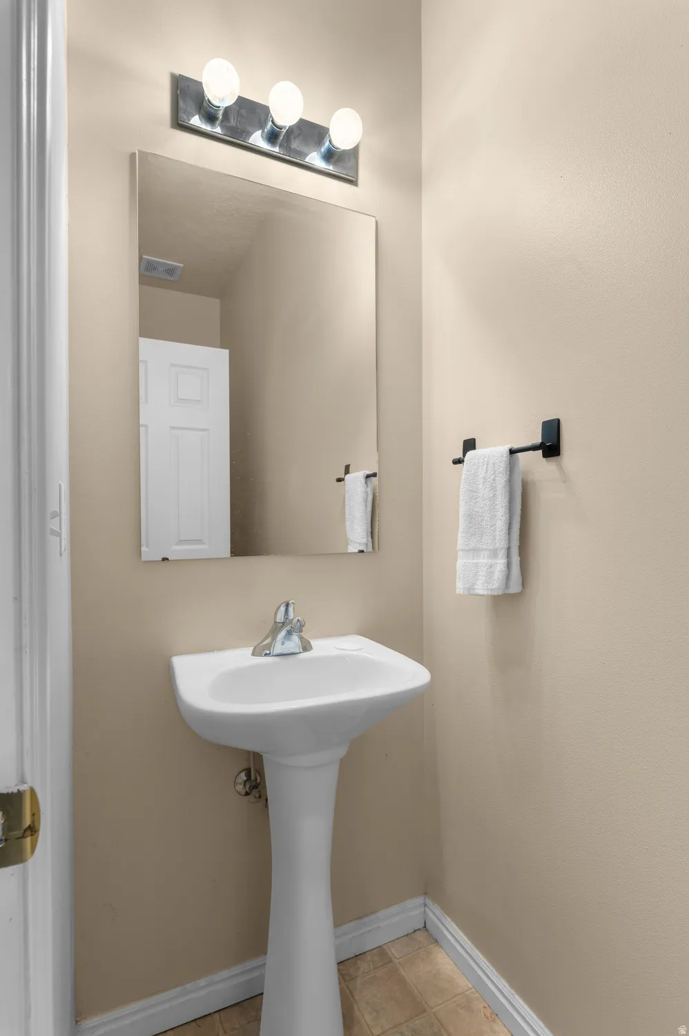 Pedestal sink with chrome faucet, large wall mirror, and modern three-bulb vanity lighting