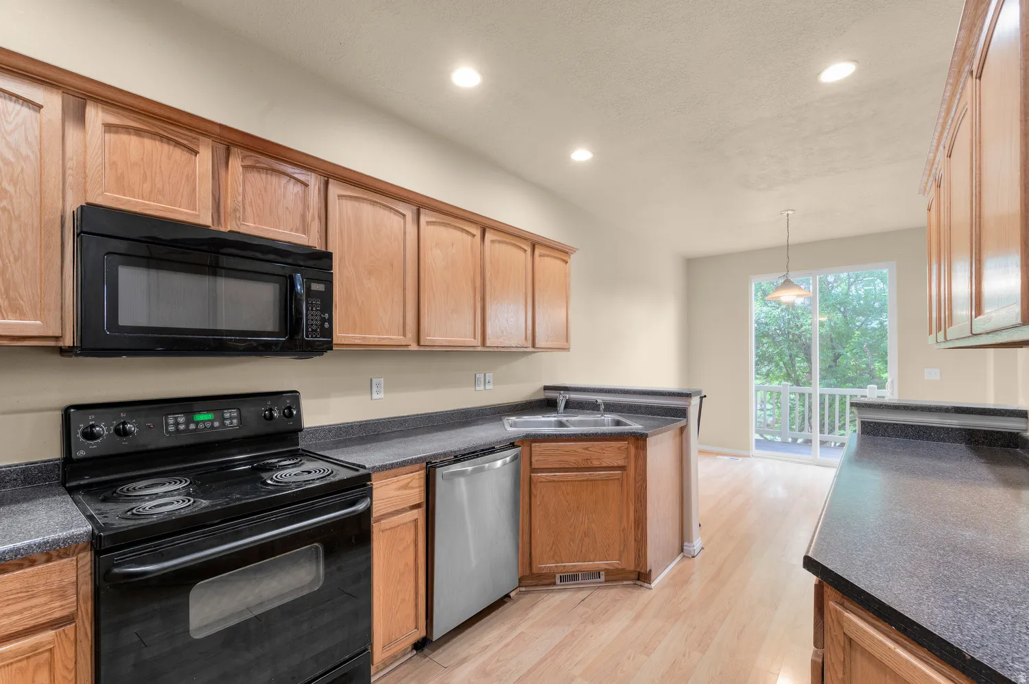 Kitchen featuring wood cabinetry, dark countertops, a black range with an overhead microwave, and a stainless steel dishwasher