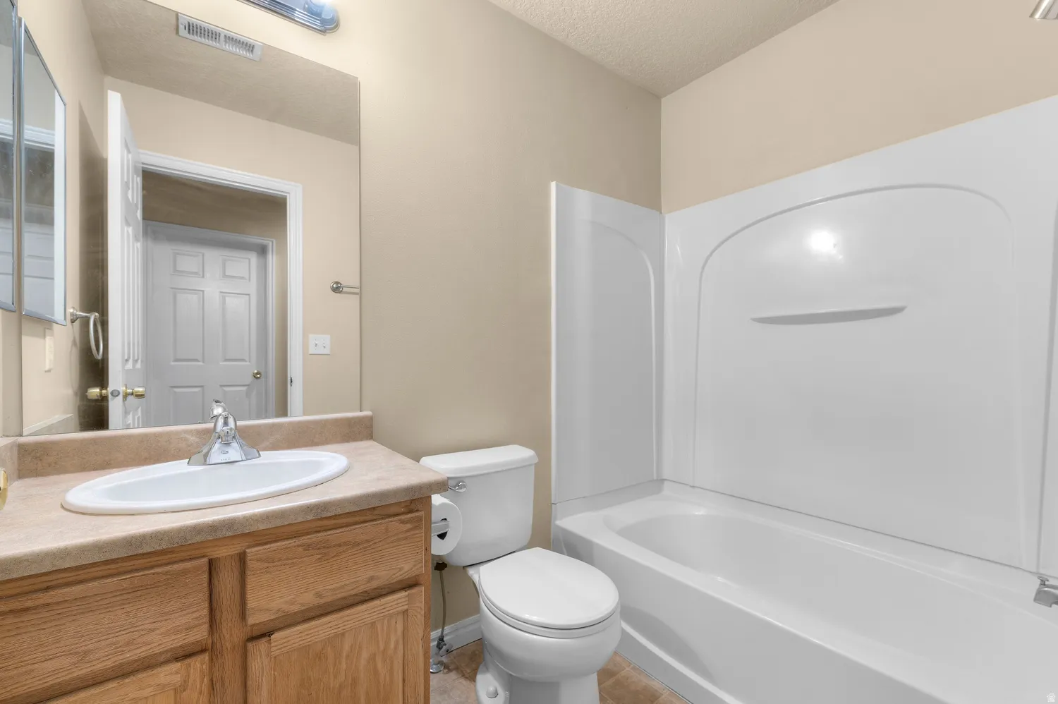 Full bathroom featuring a single vanity with wood cabinetry and a laminate countertop, an oval undermount sink, and a combination shower-tub with a white surround