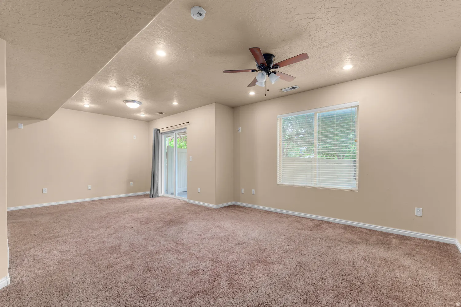 Spacious room featuring neutral carpet flooring, recessed lighting, a ceiling fan, a window with blinds, and a sliding glass door