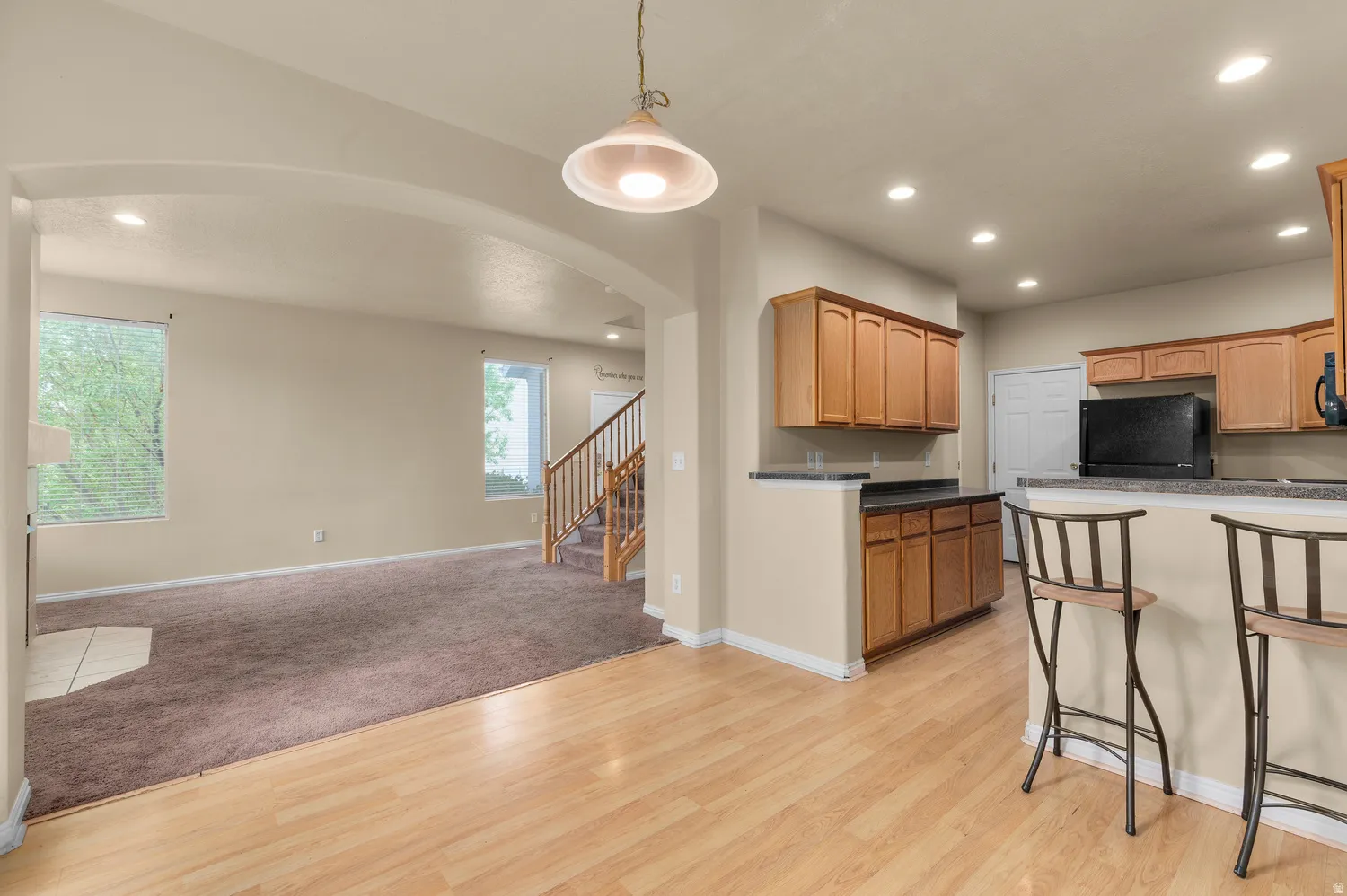 Open-concept living space featuring wood-finish flooring, a kitchen island with seating, recessed lighting, and warm wood cabinetry