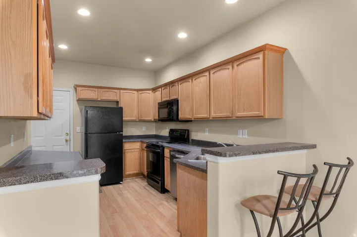 Spacious kitchen featuring wood cabinetry, dark countertops, full suite of black appliances, wood-finish flooring, and recessed lighting