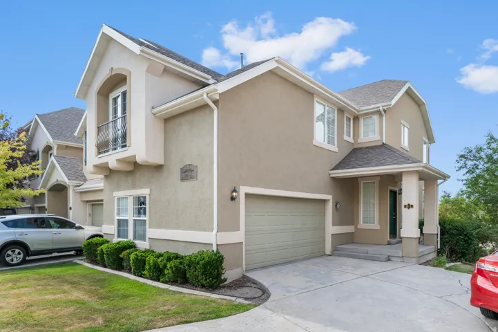 Stucco exterior with a peaked roofline, front-facing garage, covered entryway, and a Juliet balcony