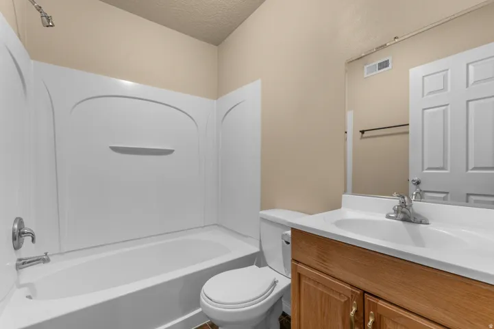Bathroom featuring a tub/shower combination with a white surround, a toilet, a wood-finish vanity with a white countertop and integrated sink, and a framed wall mirror