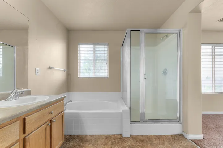 Bathroom featuring a built-in soaking tub, a separate glass-enclosed shower, a single vanity with wood-finish cabinetry, and a mirrored wall