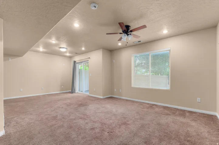 Spacious room featuring neutral carpet flooring, recessed lighting, a ceiling fan, a window with blinds, and a sliding glass door