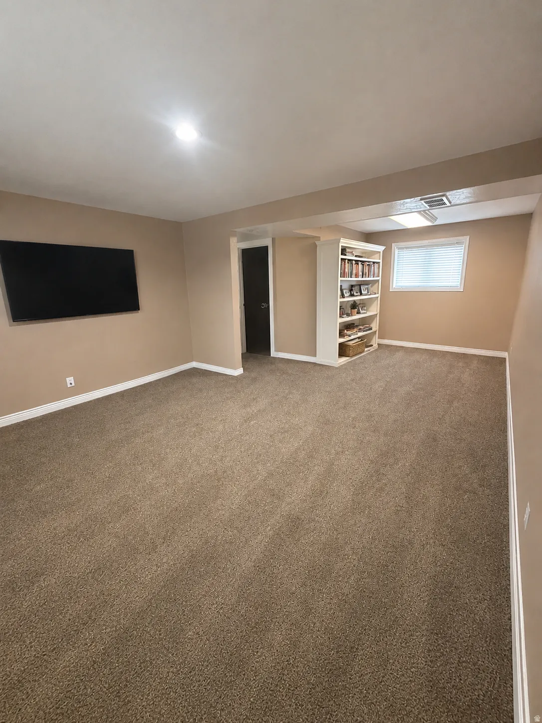 Spacious room featuring neutral carpeting, a built-in shelving unit, and a window with blinds