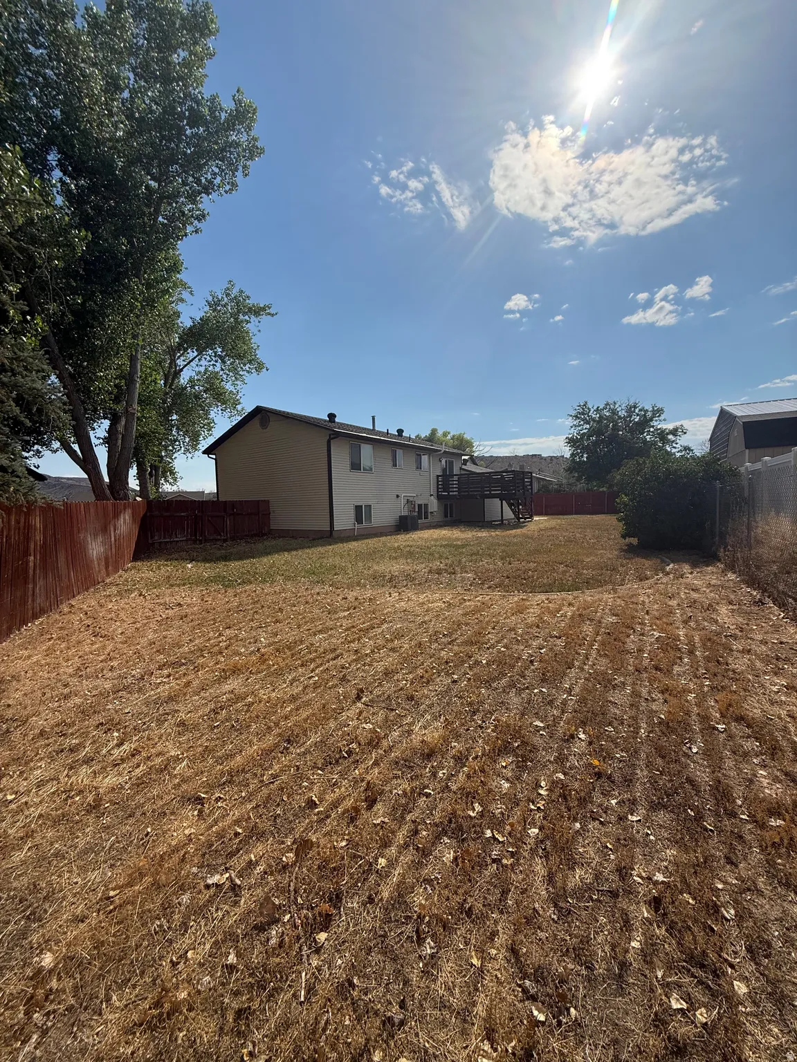 Spacious backyard featuring a multi-level wood deck, mature trees, and a full perimeter fence