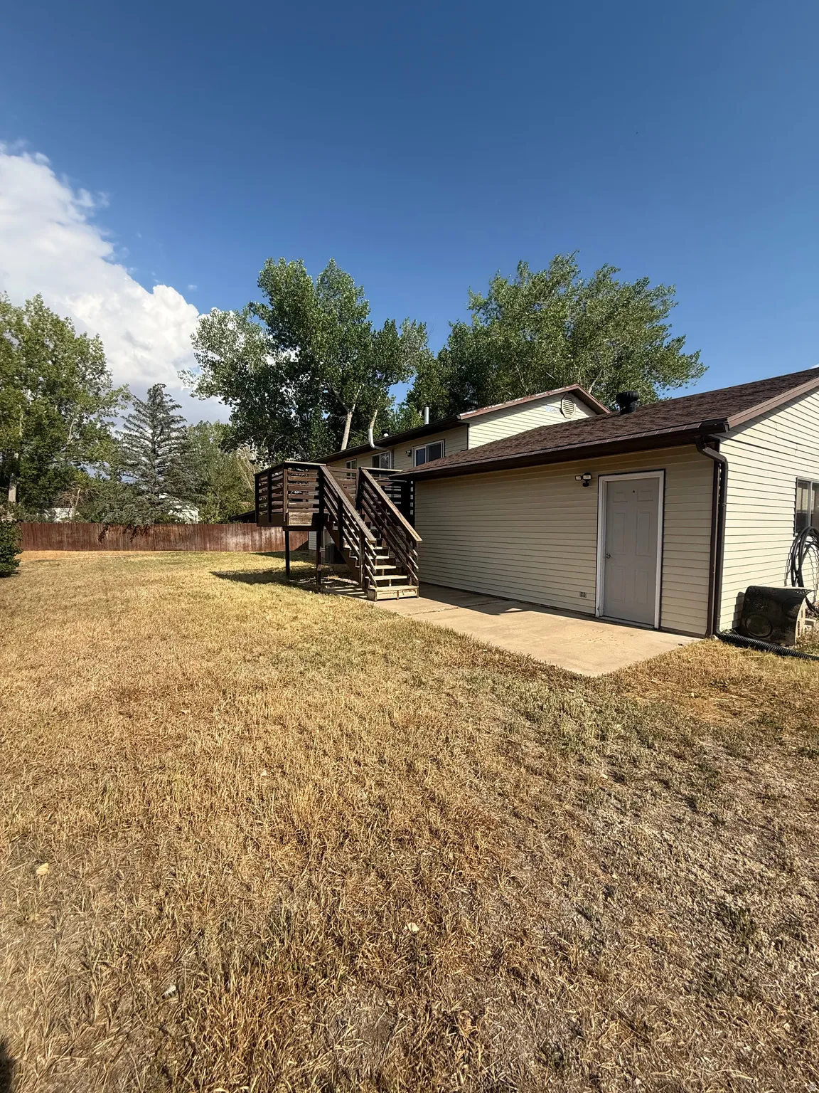 Expansive backyard featuring a multi-level wood deck, concrete patio area, and exterior access door