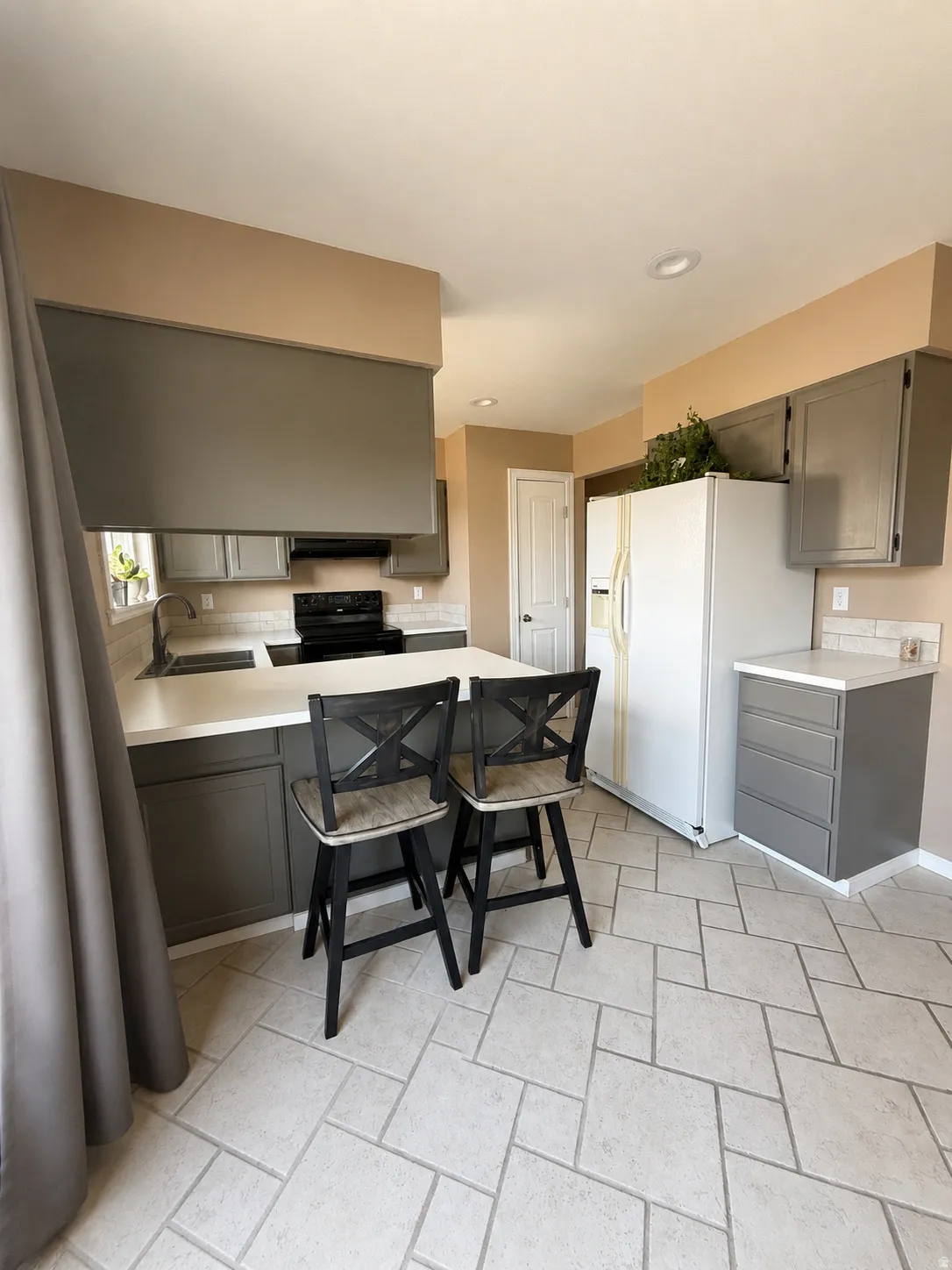 Kitchen featuring an island with countertop seating, gray cabinetry, white countertops, tile flooring, and a built-in black electric range