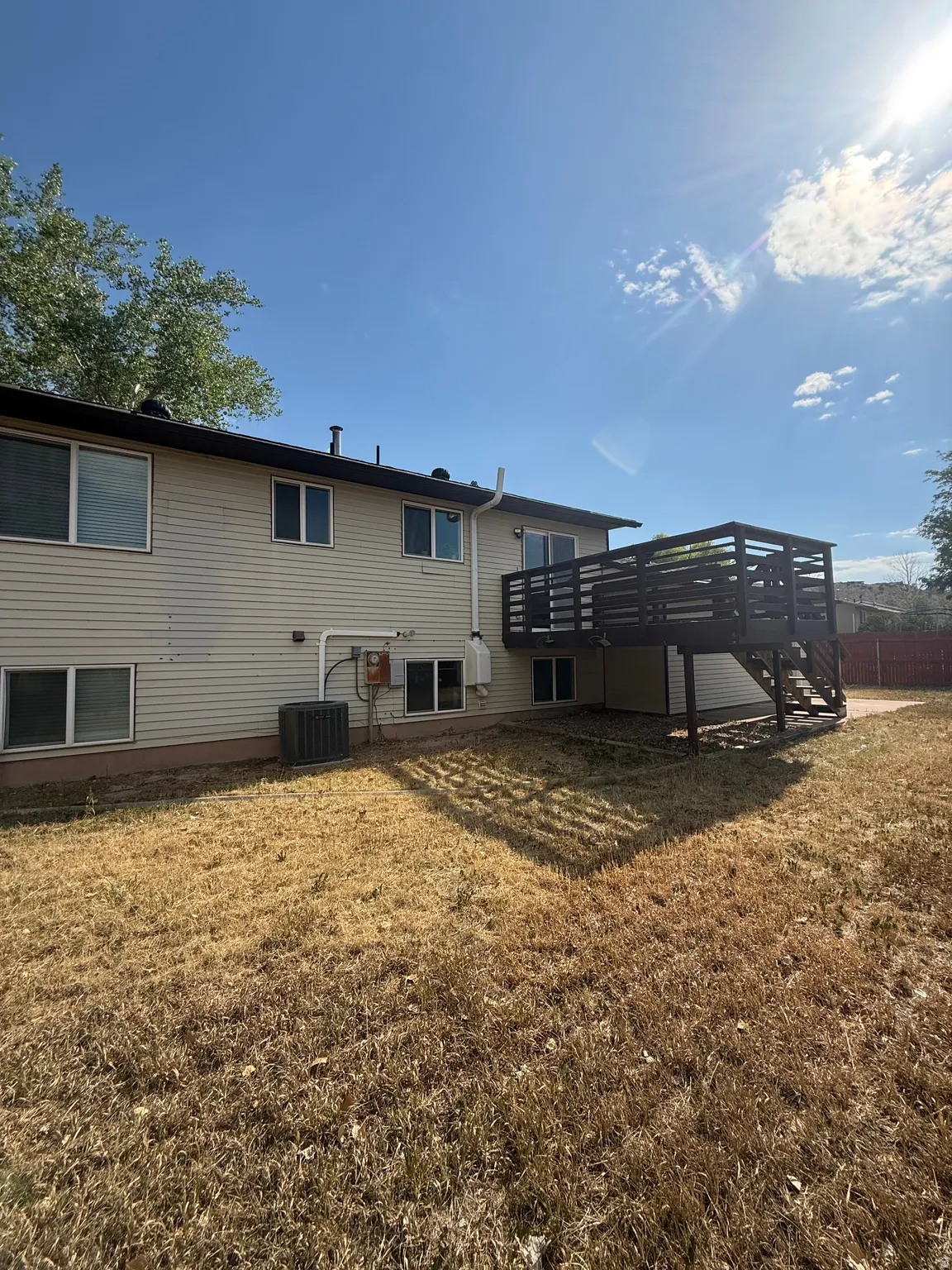 Rear exterior featuring beige siding, multiple windows, a dark-stained wood deck with privacy railing, and a ground-level patio area
