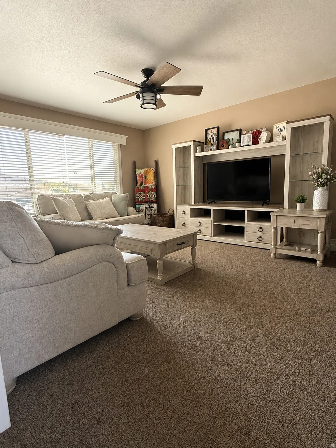 Recessed lighting and a ceiling fan with wood-finish blades illuminate the carpeted living area