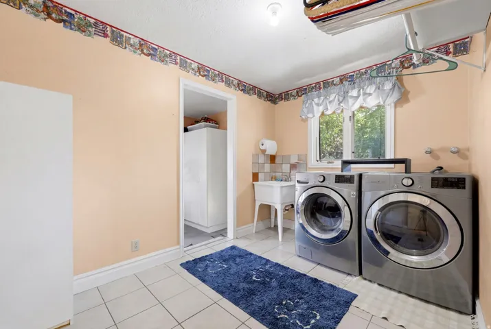 Utility room featuring tiled flooring, a double window, and an attached laundry sink with tiled backsplash
