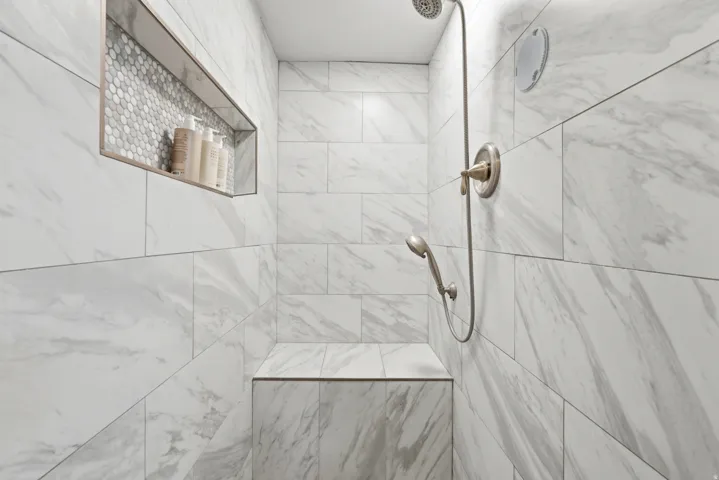Tiled shower with a built-in bench, recessed niche featuring hexagonal mosaic tile, and a brushed nickel shower fixture with a handheld sprayer