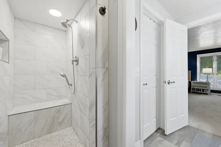 Walk-in shower featuring large format wall tiling, a built-in bench, and a recessed niche