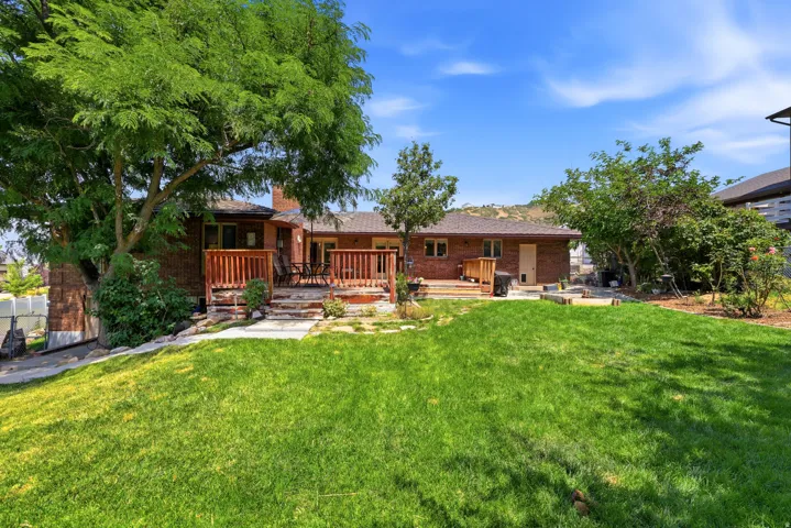 Backyard featuring a manicured lawn, multi-level wood deck, mature trees, brick exterior, and a visible chimney