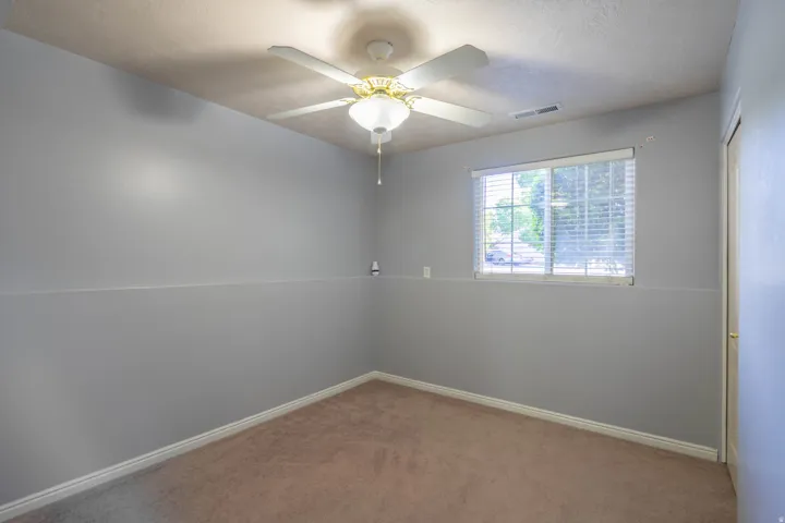Neutral-toned room featuring a ceiling fan with integrated lighting, a window with blinds, and carpeting