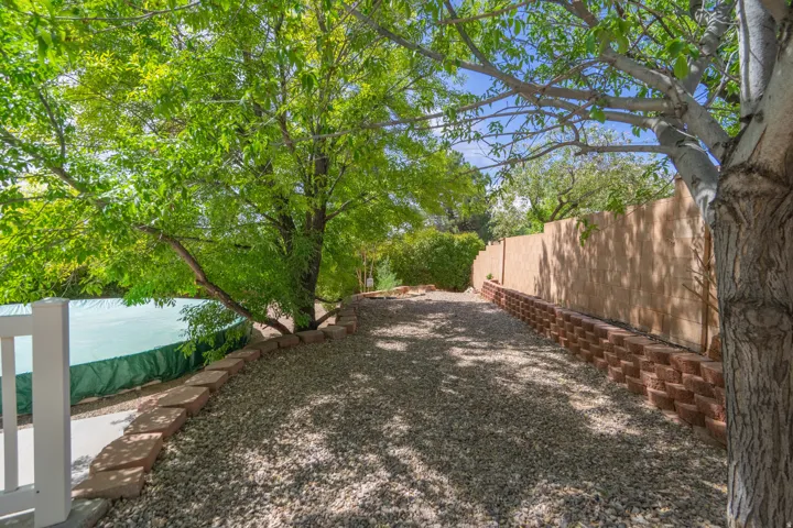 Gravel pathway bordered by a tiered retaining wall, mature trees, and a privacy fence