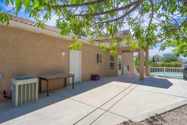 Expansive concrete patio area featuring a covered porch, stucco exterior, and a visible pool with white fencing