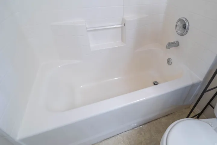 White bathtub with integrated shower, chrome fixtures, and a tiled surround