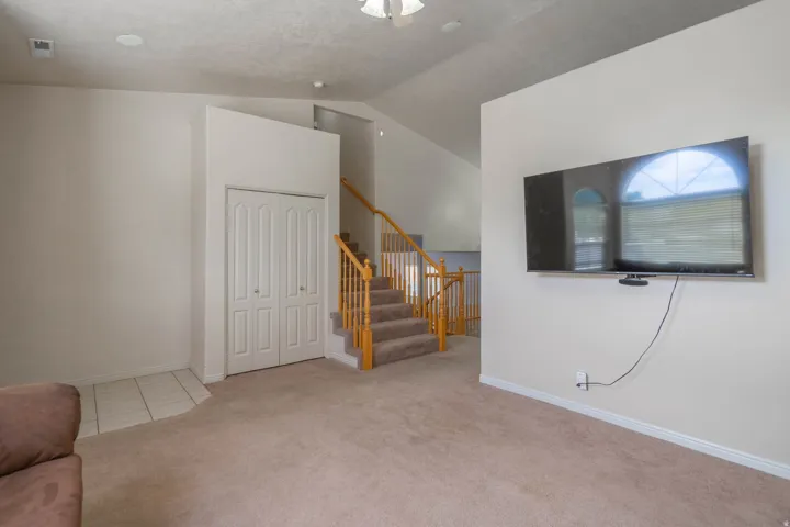 Carpeted living area featuring a vaulted ceiling and a staircase with wood balusters