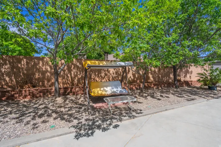 Landscaped yard featuring mature trees providing natural shade, a concrete patio area, and a privacy wall with an integrated brick retaining wall